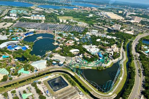 Aerial view of SeaWorld Orlando, featuring its large central lagoon, roller coasters, animal habitats, and surrounding city landscape.