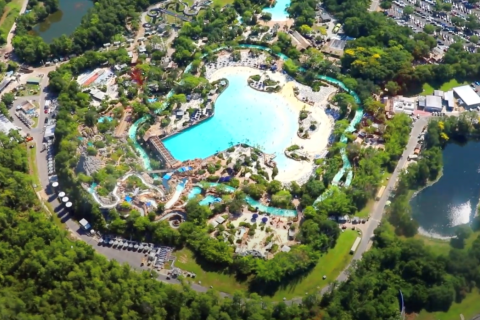 Aerial view of Disney’s Typhoon Lagoon water park, showing its large wave pool, winding lazy river, slides, lush tropical landscaping, and surrounding parking and roadways.