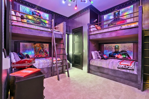 Superhero-themed bunk bedroom with four built-in beds, graphic wall art, ladders, and colorful accent lighting inside a luxury vacation home.