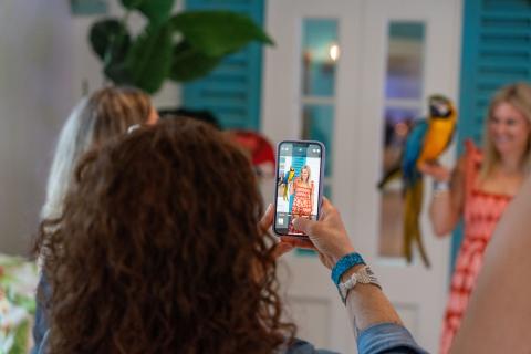 Person using a smartphone to photograph a woman holding a colorful macaw during a networking event.