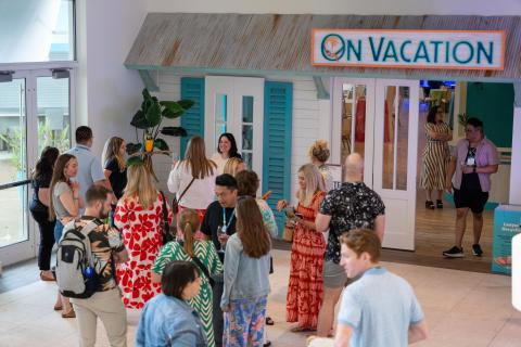 Group of conference attendees mingling in a bright indoor networking space with an “On Vacation” themed backdrop.