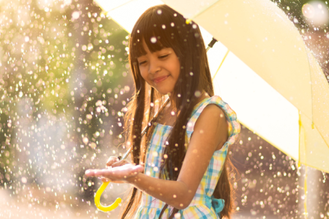Smiling girl in a sun shower with an umbrella.