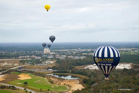 Hot air balloons drift over Kissimmee, including a blue-and-white Orlando Balloon Rides balloon flying above golf courses and neighborhoods.