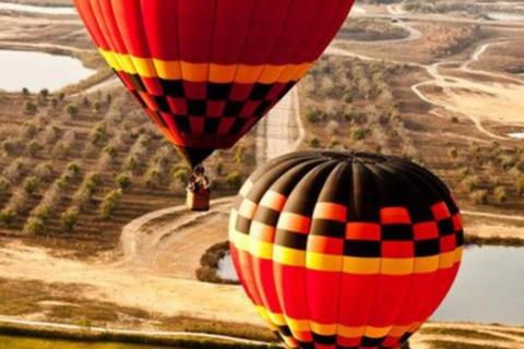 Two red balloons with a geometric pattern float above Kissimmee, Florida, with views of fields, lakes, and trees.
