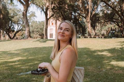 Woman standing with box of chocolates with Bok Tower peeking through old oak trees in Lake Wales, Florida.