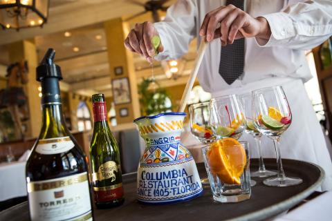 A chef prepares sangria tableside with a bottle of wine and cut fruit.