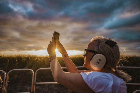 Person wearing protective earmuffs captures a glowing sunset photo while riding an airboat through the headwaters of the Everglades.