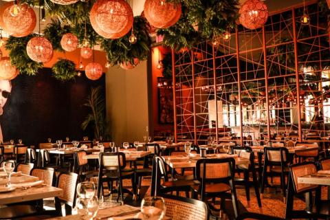 A warmly lit room with banquet seating, mirror accents, and round wicker lighting and ferns adorning the ceiling.