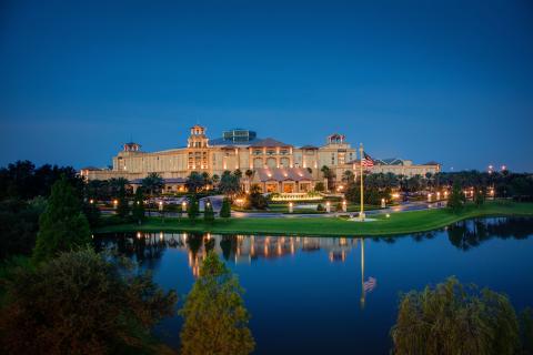 Evening view of Gaylord Palms Resort & Convention Center in Kissimmee, Florida, with the illuminated hotel reflected in the calm water and palm trees surrounding the property.