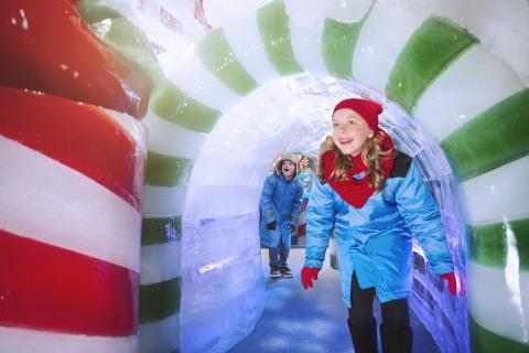 Children dressed in winter coats explore a colorful candy-striped ice tunnel at a ICE! at Gaylord Palms in Kissimmee, Florida.