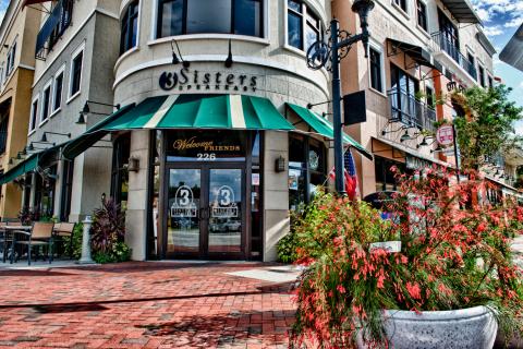Exterior of 3 Sisters Speakeasy restaurant in Downtown Kissimmee, Florida, featuring a green awning, outdoor seating, and a welcoming entrance.