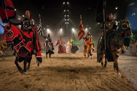 Knights in colorful armor ride on horseback carrying banners during a live performance at Medieval Times Dinner & Tournament in Kissimmee, Florida.