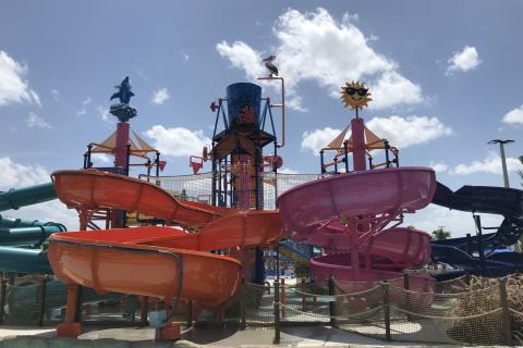 Colorful water play area with orange, pink, and blue slides at Island H2O Water Park in Kissimmee, featuring playful decorations under a sunny blue sky.
