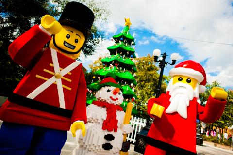 LEGO characters dressed as Santa Claus, a toy soldier, and a snowman stand in front of a large LEGO Christmas tree at LEGOLAND® Florida Resort.