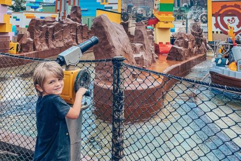 A young child smiles while aiming a water cannon at a colorful LEGO-themed water attraction at LEGOLAND® Florida Resort.