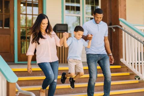 A child jumps while holding the hands of his parents