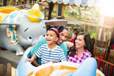 Family smiling and enjoying a ride on the Dumbo the Flying Elephant attraction at Magic Kingdom Park in Florida.
