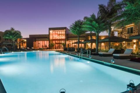 Evening view of the illuminated resort pool at Magic Village Yards in Kissimmee, Florida, surrounded by palm trees, cabanas, and elegant outdoor lighting.