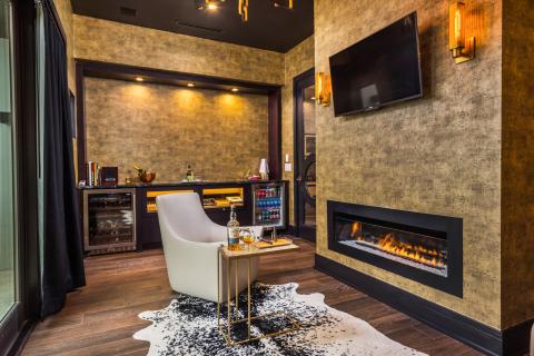 A stylish lounge area inside a Kissimmee vacation home featuring a modern fireplace, cozy armchair, mini bar, and elegant décor.