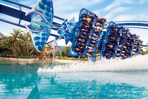 Riders soar horizontally on the Manta roller coaster at SeaWorld Orlando, skimming above a bright blue lagoon as the coaster’s wing-like trains create a dramatic splash across the water.