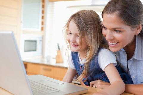 Mother and daughter smiling while planning their next family vacation on a laptop at home.