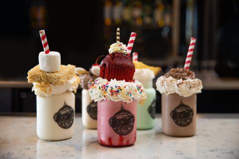 Five decadent shakes in mason jars sit on a bar. 