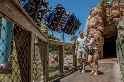 Couple at a theme park, walking on bridge with roller coaster in background
