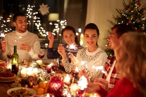Group of friends celebrating the holidays with sparklers and wine around a festive dinner table decorated with candles and Christmas lights.