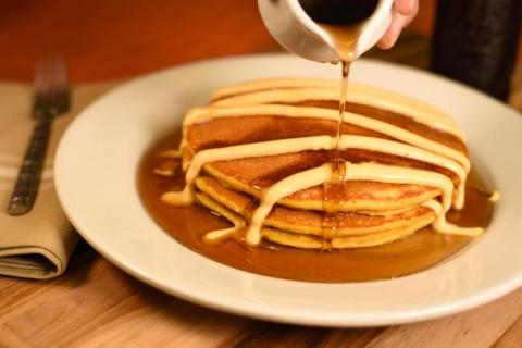 Stack of fluffy pancakes drizzled with syrup and icing on a white plate at a breakfast restaurant in Magic Kingdom.