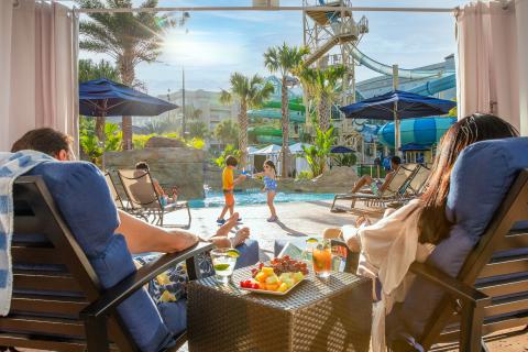 Two people lounging by the pool at the Gaylord Palms Resort and Convention Center enjoying drinks and food. 