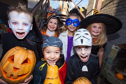 A group of smiling children dressed in Halloween costumes pose together holding pumpkins, ready for a night of trick-or-treating and fun.