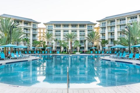 Resort-style pool with turquoise water, palm trees, lounge chairs, and multi-story hotel buildings at Margaritaville Resort Orlando.