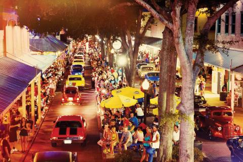 Crowds gather along Main Street in Old Town Entertainment District in Kissimmee, Florida, to watch a classic car cruise featuring vintage vehicles at night.