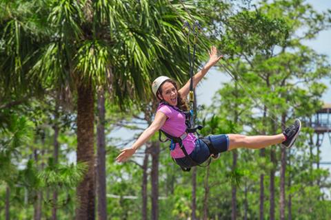 A woman ziplines through the trees in Florida, very happy.