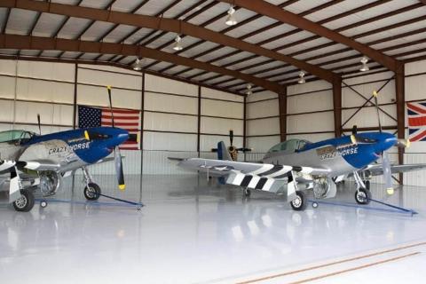 Two silver and blue P-51 Mustang aircraft named “Crazy Horse” parked inside a polished hangar in Kissimmee, Florida, adorned with American and British flags.