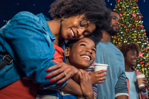 Family enjoying a festive evening with hot cocoa and holiday lights in front of a decorated Christmas tree at Universal Orlando Resort.