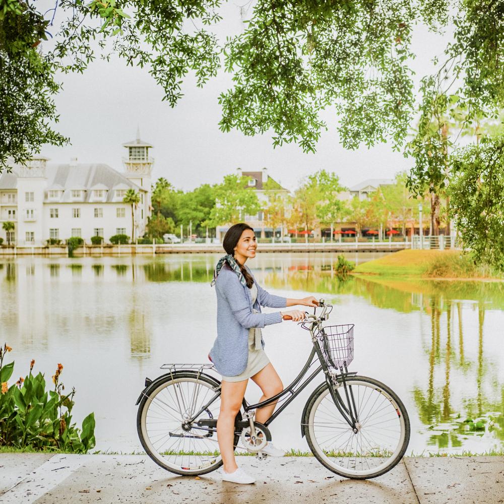 Woman smiling while standing beside her bicycle along a scenic lakeside path in Celebration, Florida.