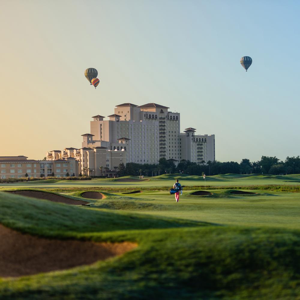 Golfer golfing at sunset at the Omni Orlando Resort at ChampionsGate in Kissimmee, Florida, with hot air balloons flying overhead.