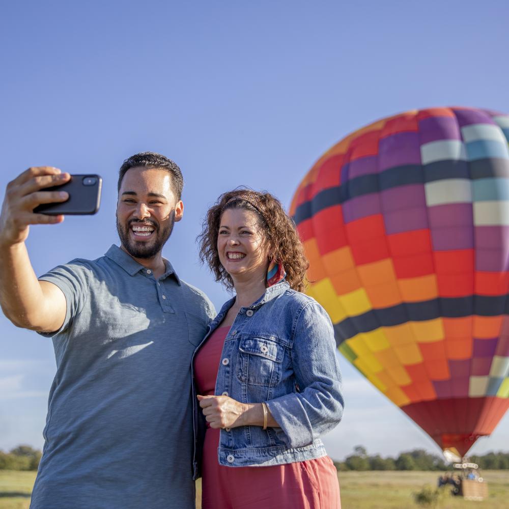 Couple taking a selfie in front of the hot air balloon in a field