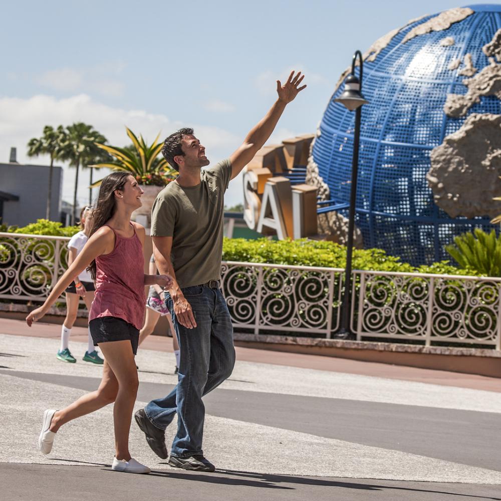 Couple walking and smiling near the iconic Universal globe at Universal Orlando Resort on a sunny day in Central Florida.