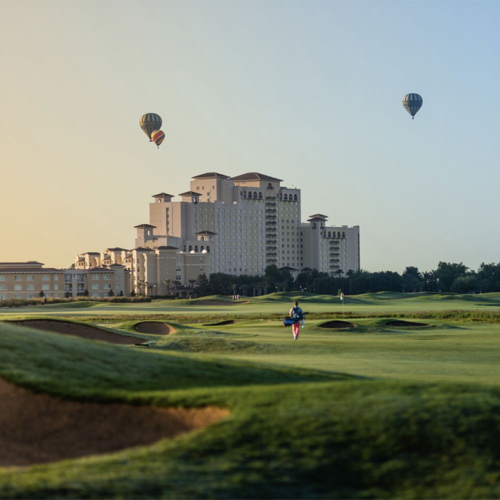 Hot air balloons fly over the Omni Orlando Resort at ChampionsGate at sunset. Golf course is in foreground.