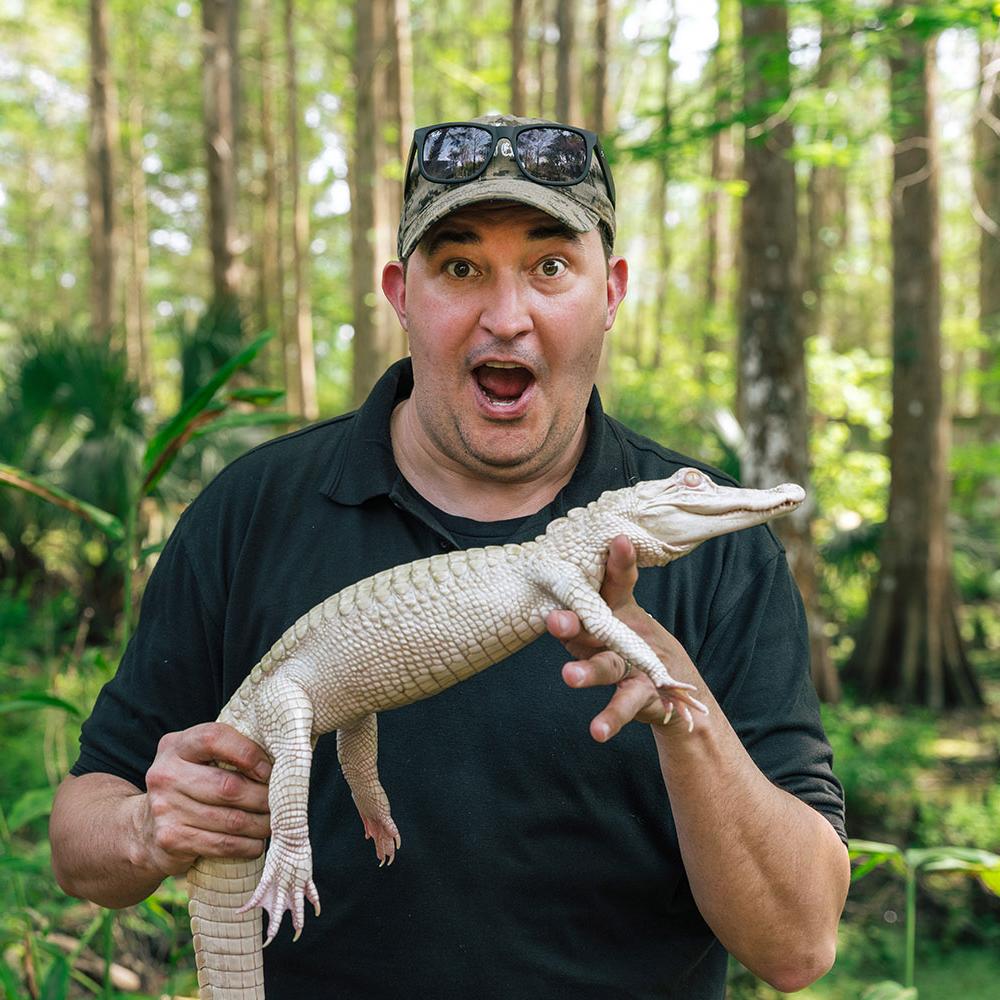 Jeff Musial holds an albino alligator in front of the trees at Wild Florida.