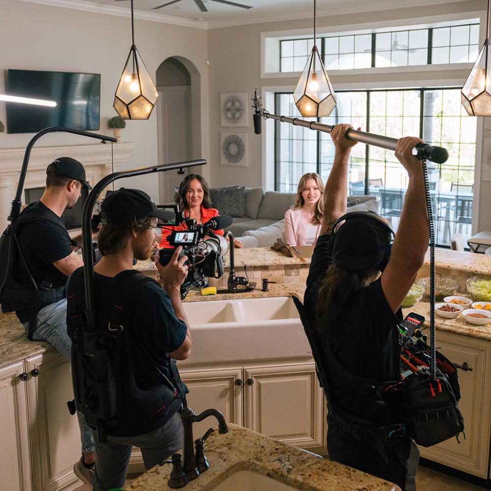 Jen and Kyla sitting at the kitchen island with the camera guys holding equipment for filming