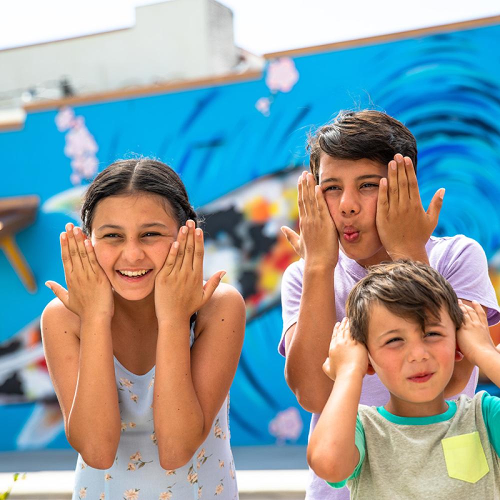 Three children smile and make playful faces while standing in front of a bright, colorful fish mural in Kissimmee.