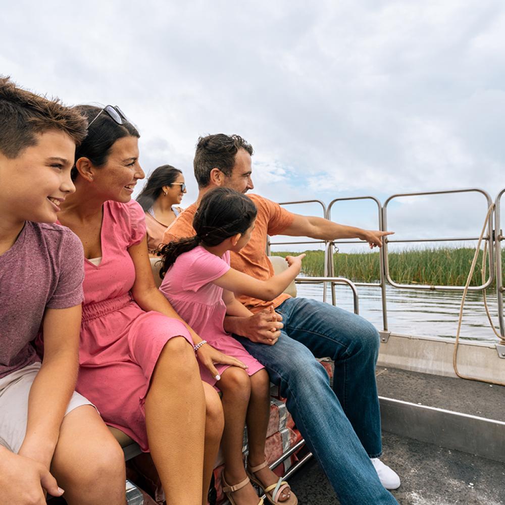 A family enjoys an airboat ride through the wetlands at Wild Florida, smiling and pointing at wildlife in the distance.