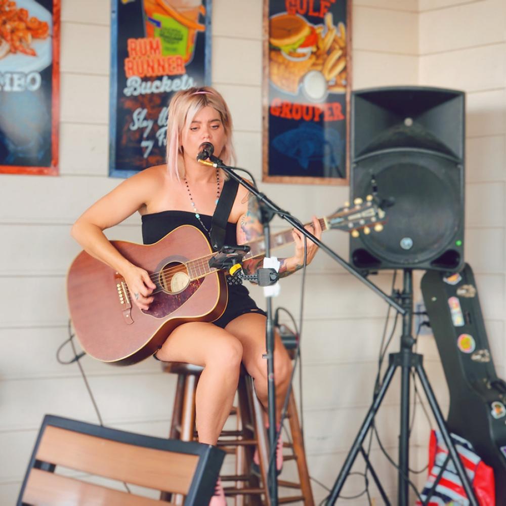Musician performing live acoustic guitar and vocals at Crabby Bill’s in St. Cloud, Florida, with colorful seafood-themed posters in the background.