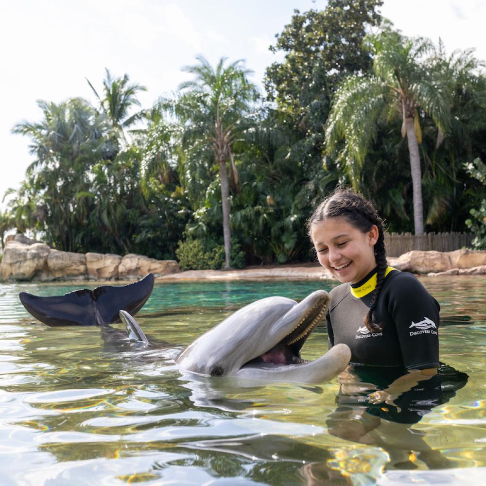 Young girl with brown hair swims with a dolphin at Seaworld Discovery Cove in Orlando, Florida