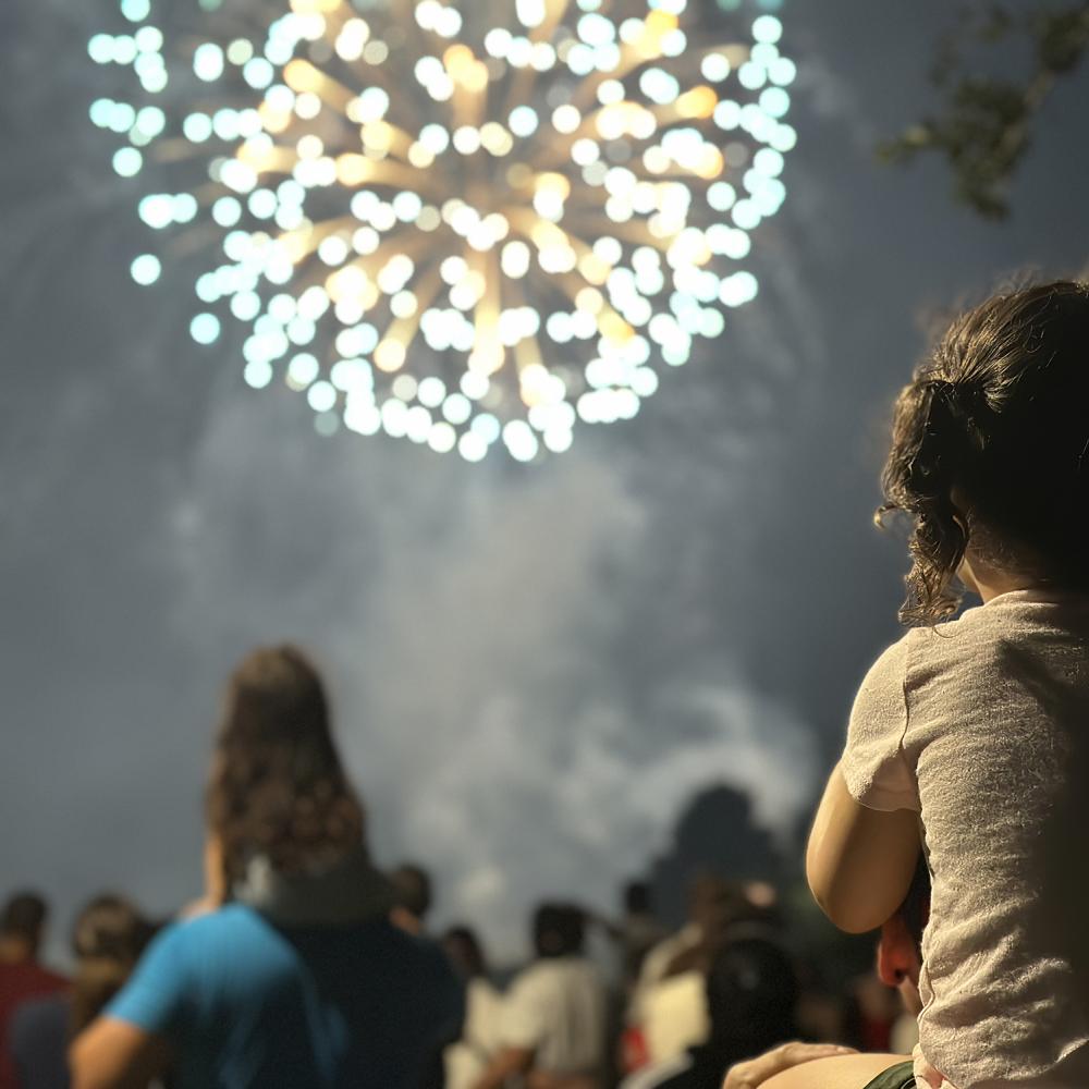 A young girl on her father's shoulders looking at fireworks in a crowd in Celebration, Florida.