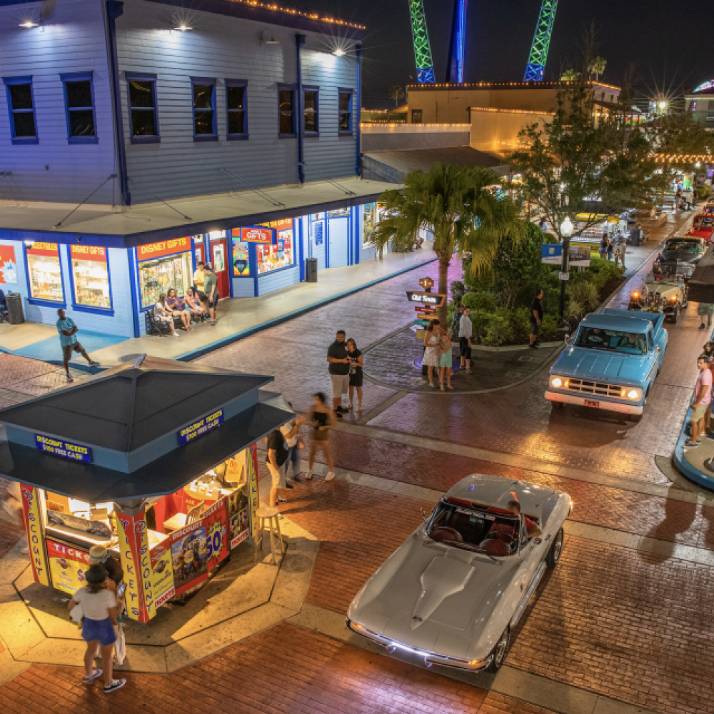 Nighttime scene at Old Town Kissimmee featuring classic cars cruising down the brick streets, colorful shops, and visitors enjoying the lively atmosphere.