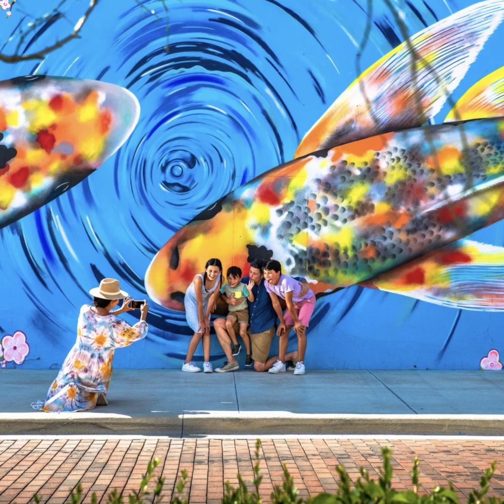 A family poses for a photo in front of a large, colorful koi fish mural in Kissimmee while someone kneels to take their picture.